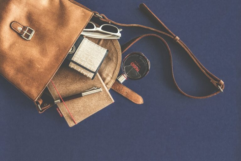 Stylish flat lay of a leather handbag with luxury accessories including sunglasses, wallet, notebook, and pen.
