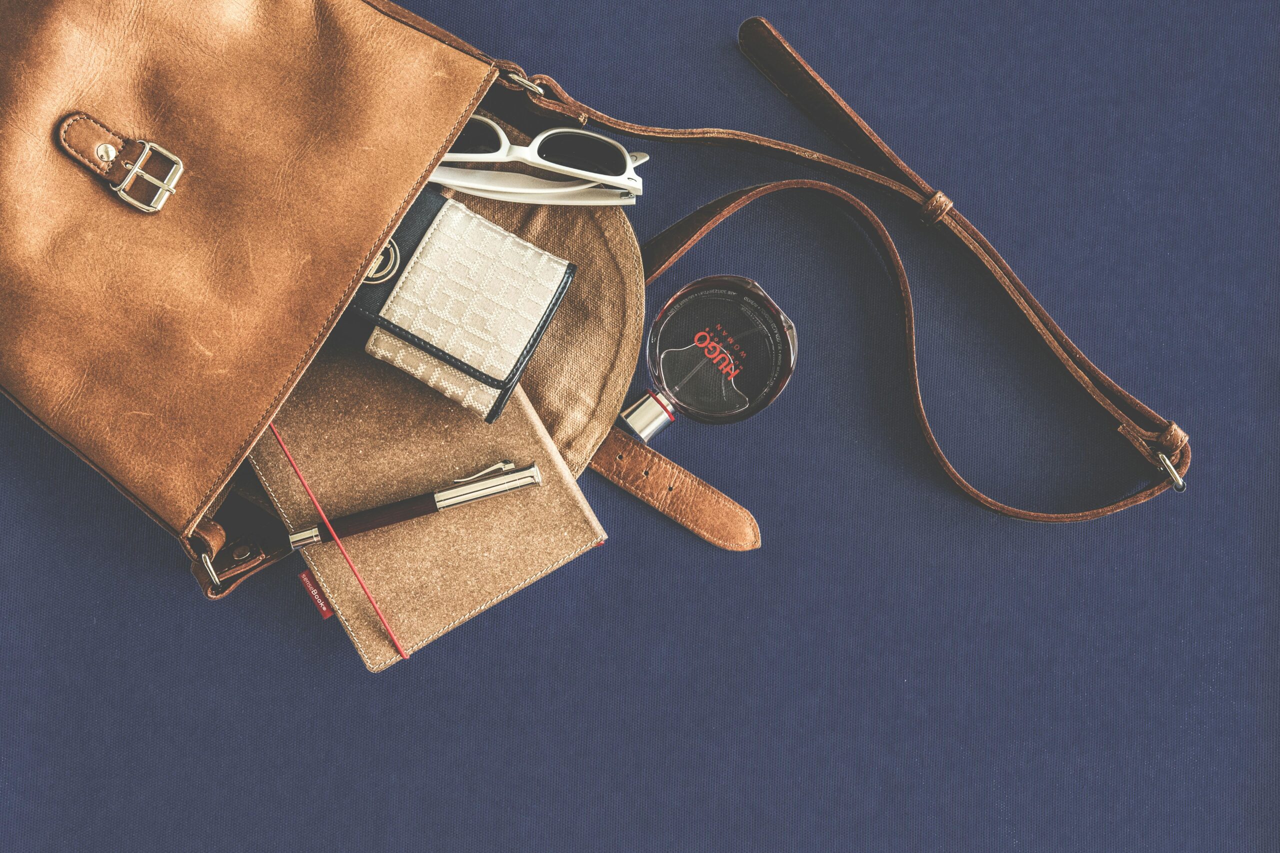 Stylish flat lay of a leather handbag with luxury accessories including sunglasses, wallet, notebook, and pen.
